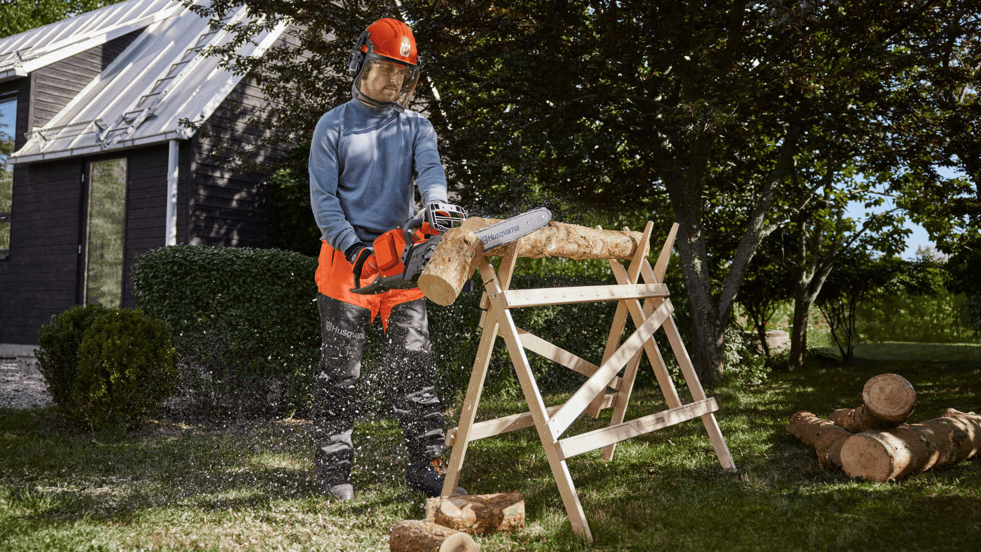 man sawing tree trunk with chainsaw whilst wearing protective gear in backyard